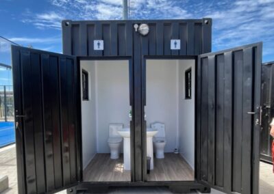 Container converted into portable toilets with open doors, blue sky background.
